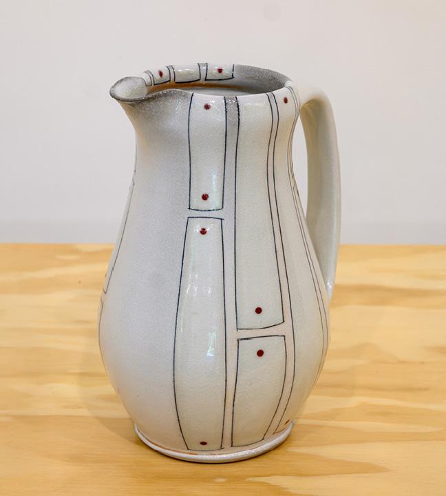 an off-white ceramic pitcher decorated with gray rectangles and brownish-orange dots 