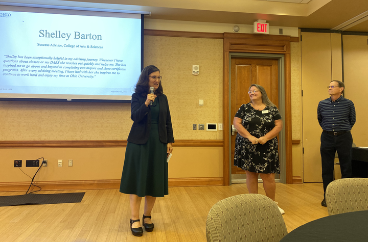 Jenny Klein speaks about Shelley Barton, while Barton and David Descutner stand nearby at the awards ceremony