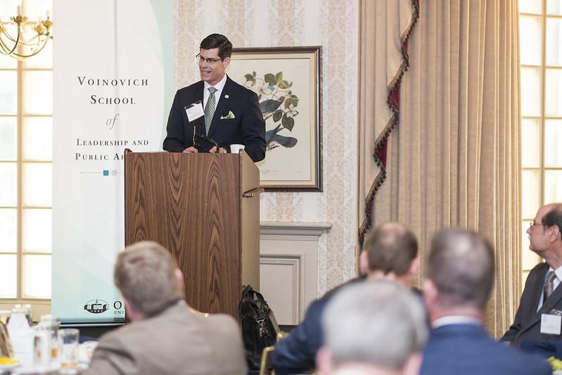 Mike Adelman gives a presentation at a podium at a Voinovich School event