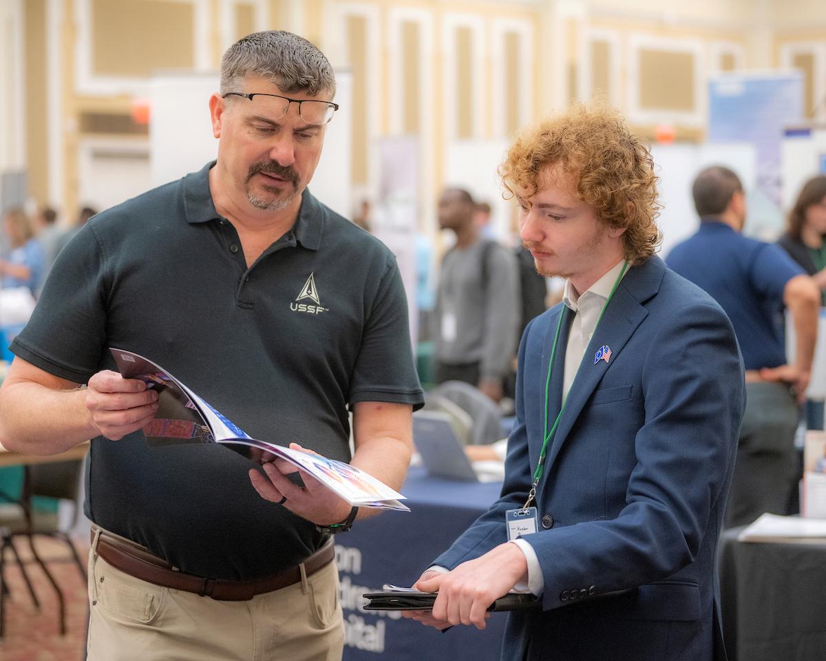 An OHIO student talks with a business  representative and looks through a brochure at the Career Fair in the Baker University Center Ballroom
