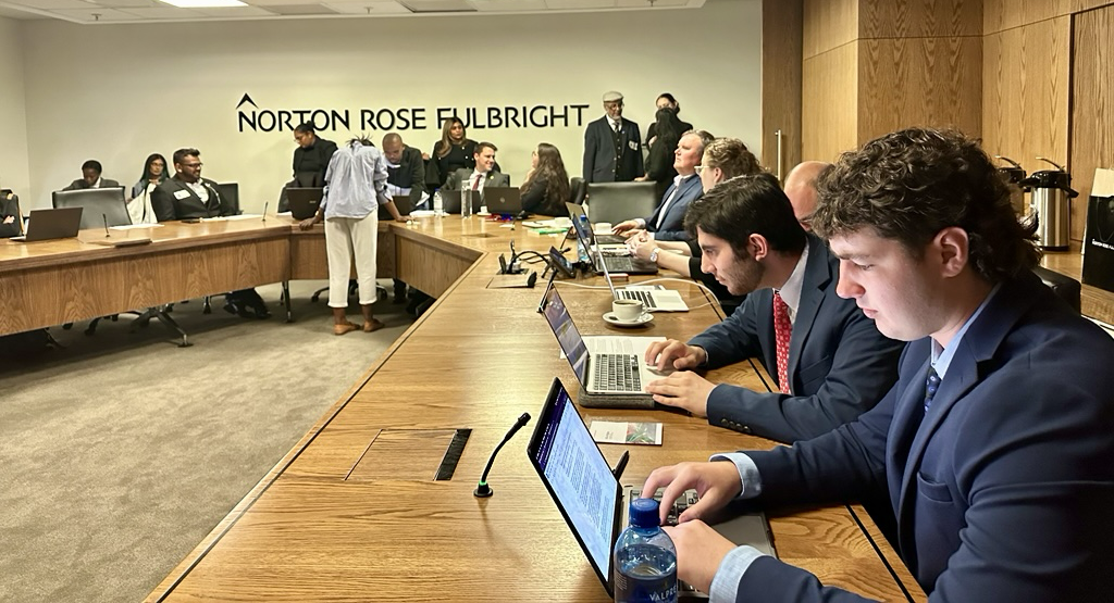 OHIO students dressed in professional attire work on computers in a room that has the words "Norton Rose Fulbright" on the wall