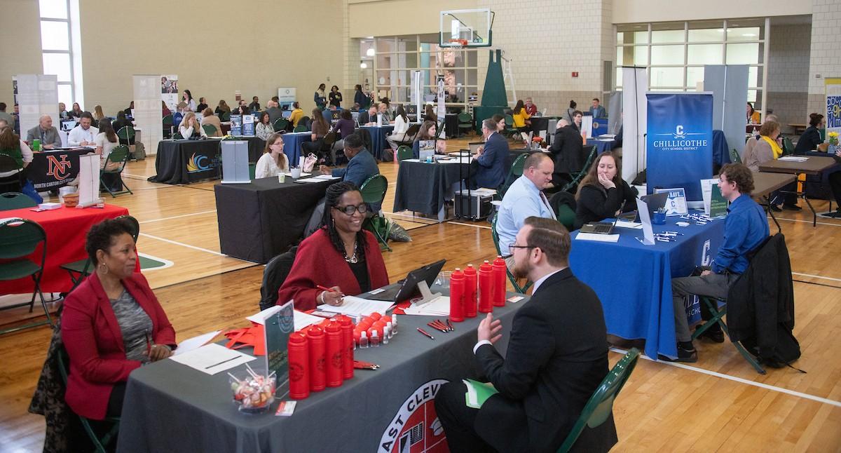 OHIO students sit at tables talking with school district representatives about jobs at the Education Career Fair, held in a gymansium at OHIO
