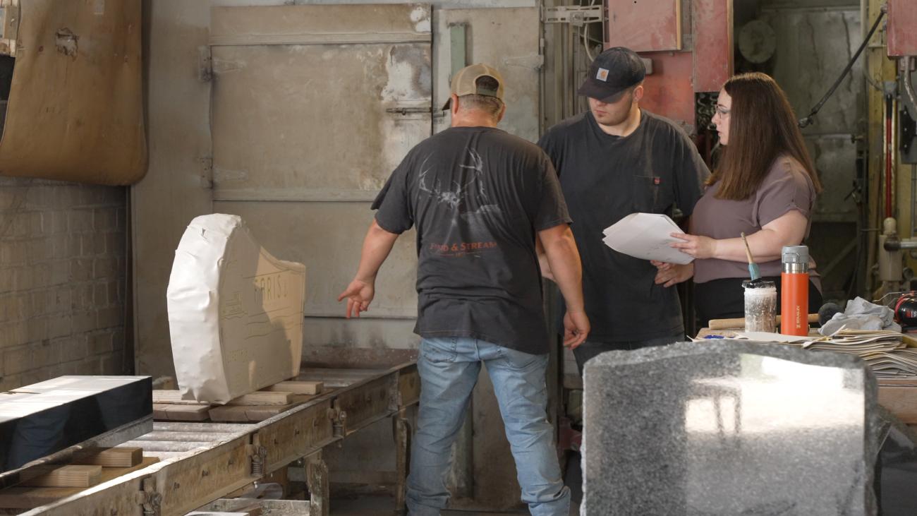 Representatives from the Logan Monument Company and the Small Business Development Center talk while looking at a monument in a room at the business.