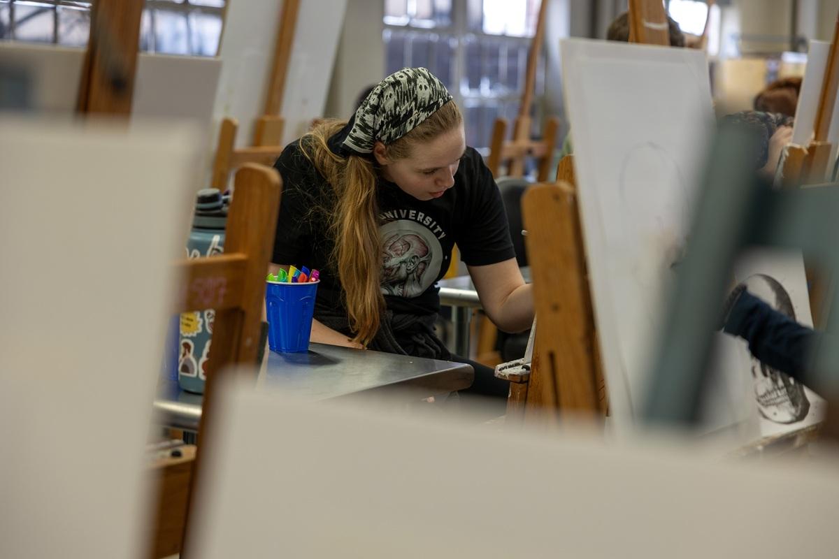 An OHIO student paints on an easel while surrounded by several other easels