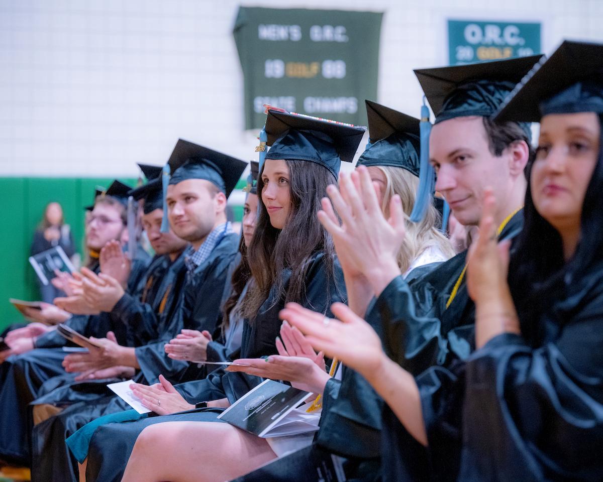 Graduates seated during the Graduation Recognition Ceremony clap for a speaker.