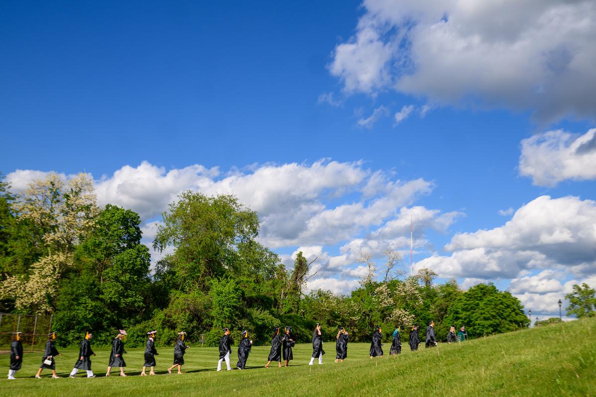 OHIO graduates walk in a line down a path through the green grass while wearing their caps and gowns before the Graduation Recognition Ceremony at Ohio University Chillicothe