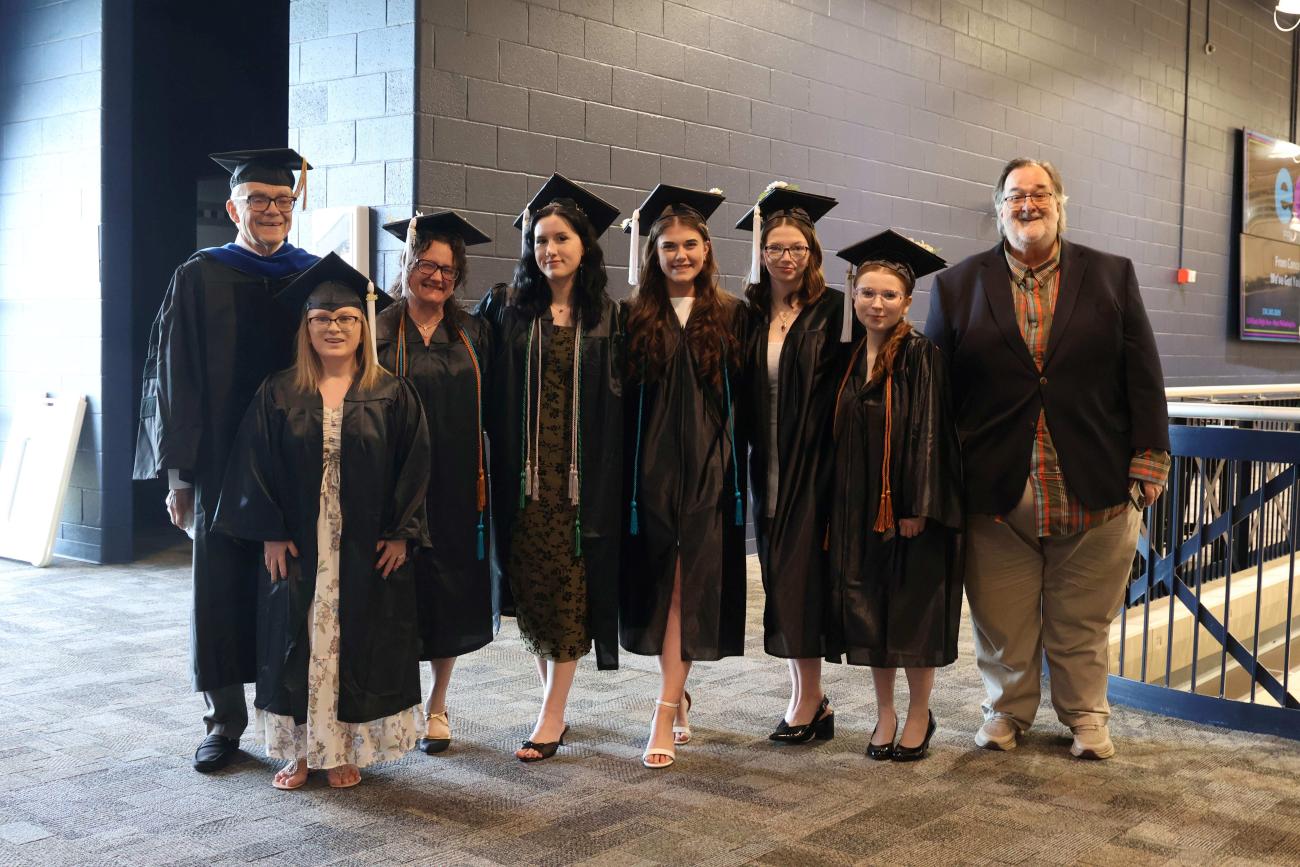 Professors and Graduates dressed in regalia, standing in a line, smiling