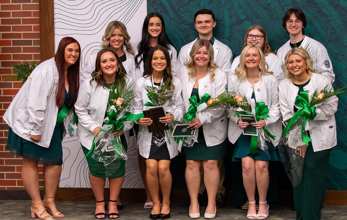 The students in the Class of 2026 stand together while wearing white coats and holding flowers at the pinning ceremony