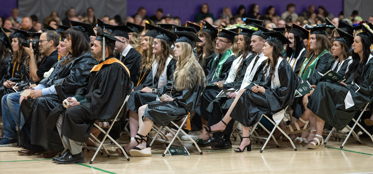 OHIO graduates sit together in rows of chairs while wearing their caps and gowns during the Graduation Recognition Ceremony inside a gymnasium at Ohio University Zanesville.