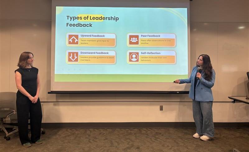 Two OHIO students lead a presentation and the screen behind them says "Types of Leadership Feedback"