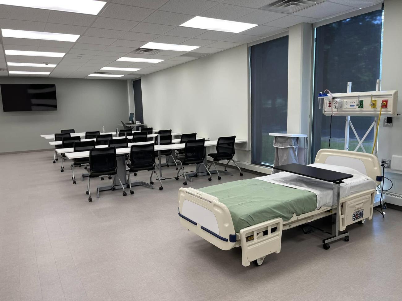 A hospital bed and tables and chairs are shown in the new nursing lab