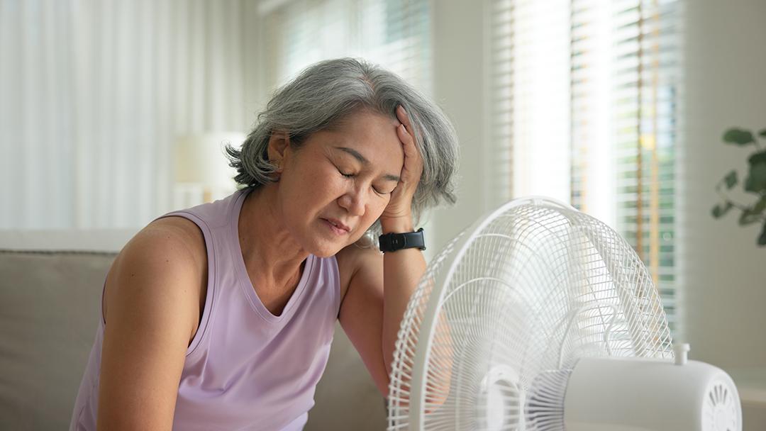 A woman is overheated and sits in front of a fan to cool off.