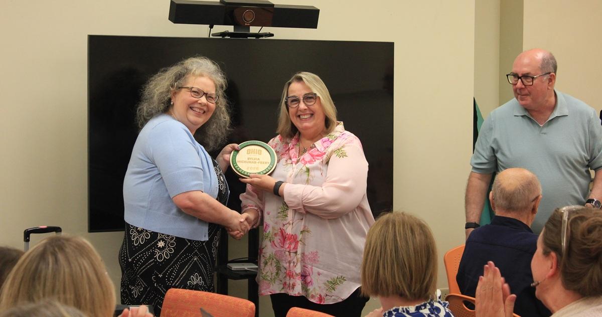 Two employees from the OHIO Business Service Center hold an award while the audience applauds