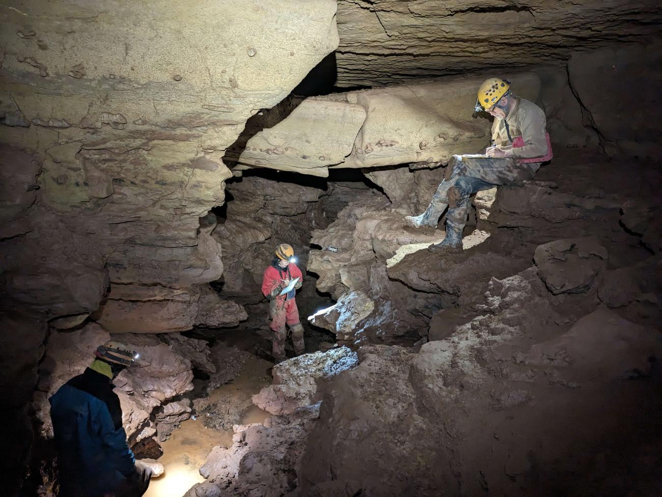 An OHIO student stands deep in a cave working on a research project, while two other individuals are nearby