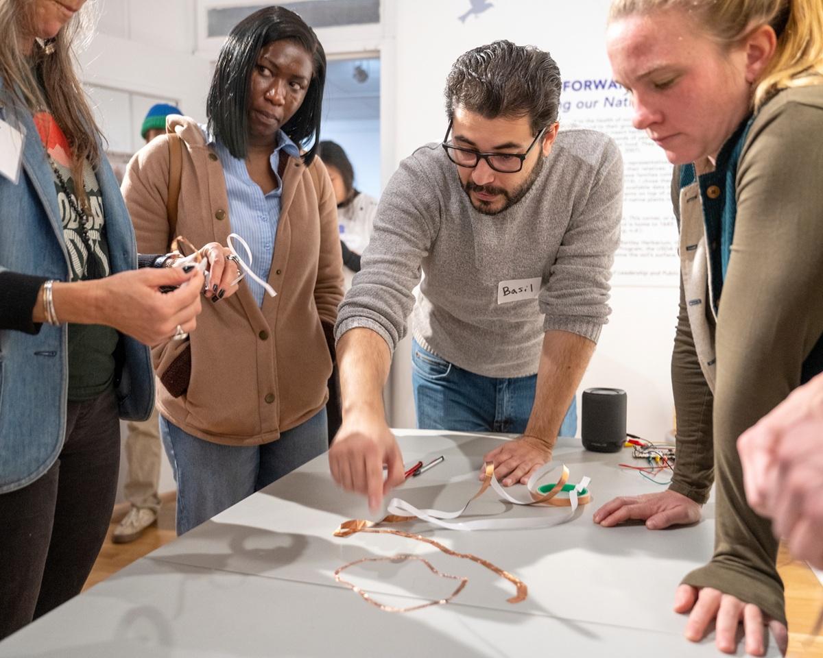 An OHIO faculty member leads a presentation on a table while people watch nearby