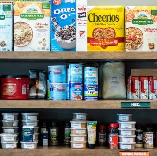 A photo of food pantry shelves filled with cereals, canned good, baking items, spices, coffee and other items