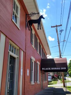 Two story red brick building, with a black awning over the entrance and a large black iron horse mounted near the entrance