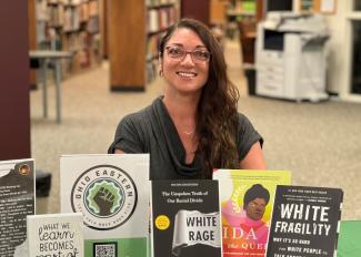 White female with long brown curly hair sitting behind a table that has books propped up in book stands