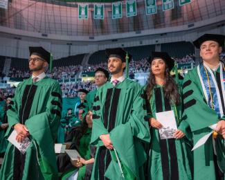 Students stand during HCOM commencement ceremony.
