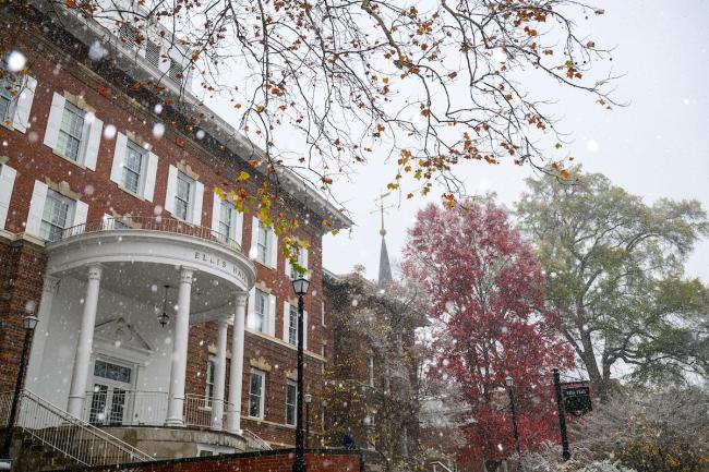 Ellis Hall is surrounded by colorful trees while snow falls on OHIO's College Green