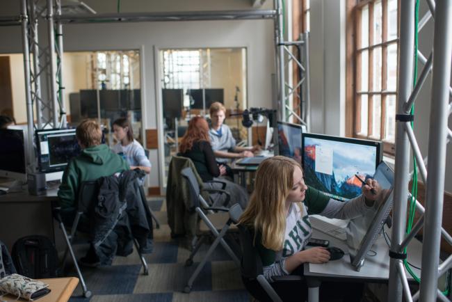 Students working at computers in an office space-like classroom.