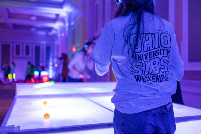 An OHIO student wears a shirt that says Ohio University Sibs Weekend while playing ping pong at the GLOHIO event in the Baker University Center during Sibs Weekend 2025.