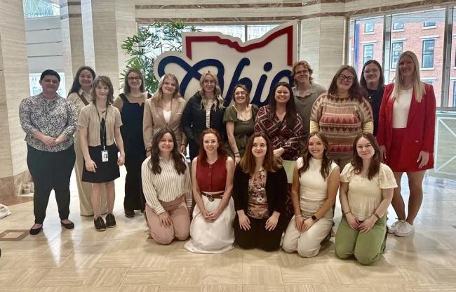A group of OHIO students and faculty stand in front of an Ohio sign while at the Ohio Statehouse for Advocacy Day.