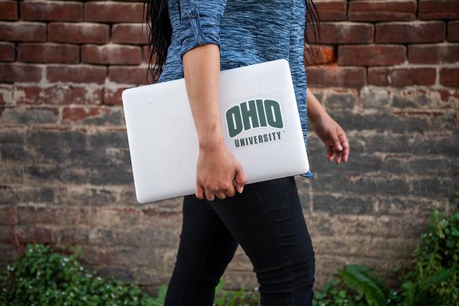 An OHIO Online student walks with a laptop with the Ohio University logo on it.