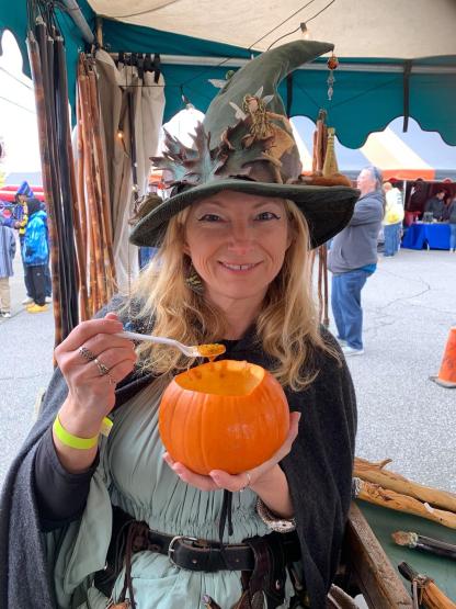 An individual in wizard costume is shown  eating food out of a pumpkin at a booth at Wizardfest