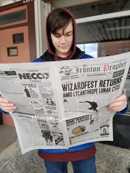 An individual is shown reading the Ironton Prophet newspaper at Wizardfest