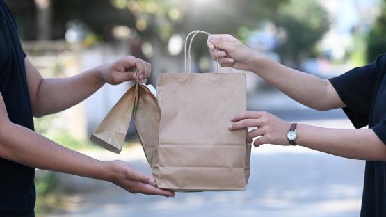 two people off screen hand off and receive a paper bag as in a food delivery