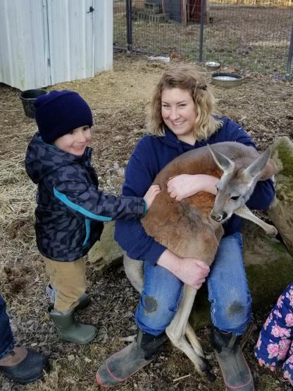 Sara McClaskey holds a kangaroo while a small child pets the animal and smiles