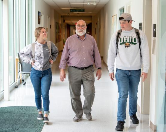 Two Ohio University students walk down a hallway with an OHIO faculty member