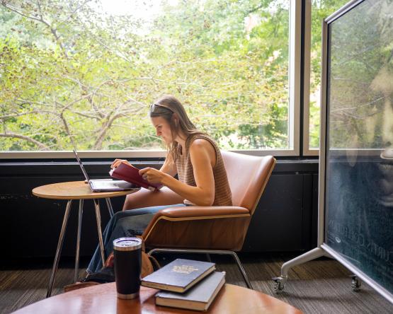 An OHIO student reads a book near a window while sitting at a table in Alden Library