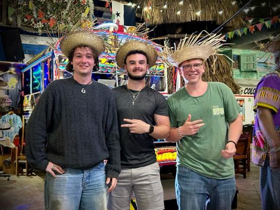 Caleb Buck and two other OHIO students wear straw hats at an outdoor festival