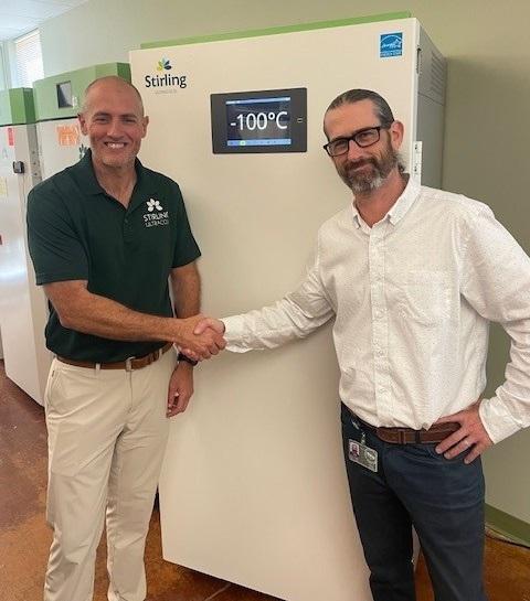 Clayton Newman and Andrew Tucker shake hands while standing in front of the VAULT100 ULT freezer in the Ohio University Innovation Center