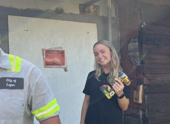 Sydney Roseberry holds a drill while standing outside of a house