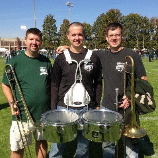 The Voytek brothers stand together with their musical instruments while wearing Marching 110 Alumni clothing items