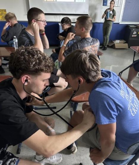 High school students practice using a stethoscope.