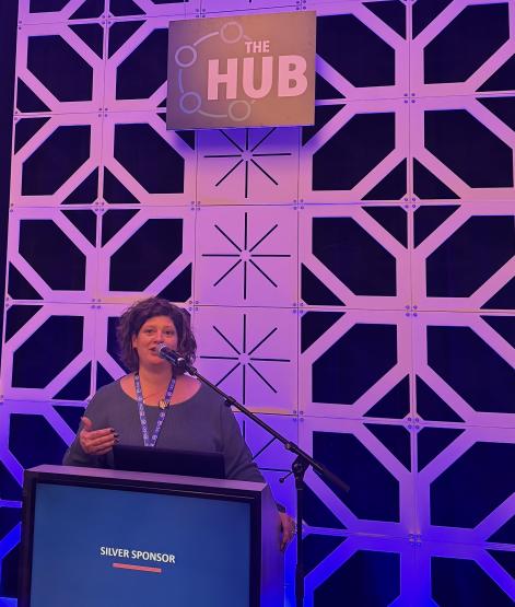 Andrea Lewis speaks at a podium with blue and purple colors behind her at a national event