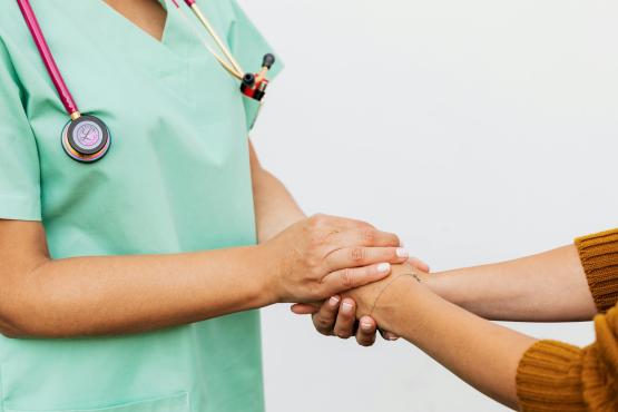 A health care worker in green scrubs gently holding a patient’s hands