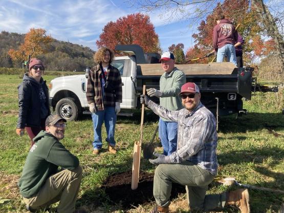 Volunteers pose for a photo in front of a truck and a tree during the tree planting event