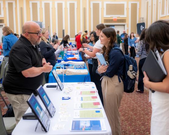 An OHIO student talks with a business representative, while many other students are also shown in the background talking with business representatives at the Career Fair in the Baker University Center Ballroom.