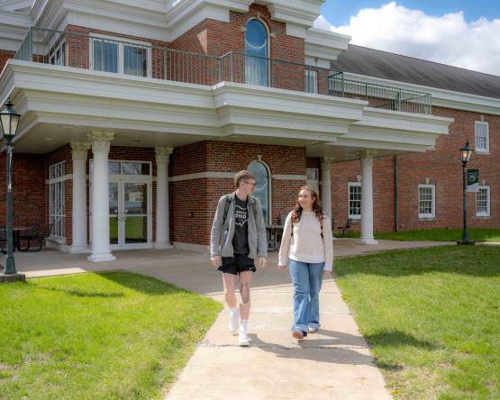A male and female walking next to each other walking down a sidewalk, outside the rear entrance to Ohio University Eastern Shannon Hall