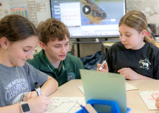 two female students drawing, one male teacher overlooking their work