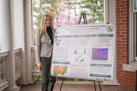 A Voinovich Research Scholar stands by research presentation poster