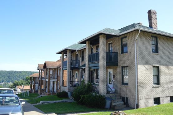 A row of two-story housing units with cars parked in the street in front.