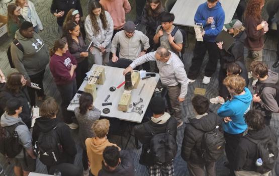 A Learning Community instructor works on a project at a table while a large crowd of students watches