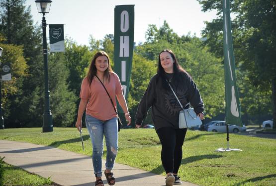 Two female students walking side by side on a sidewalk on a sunny day