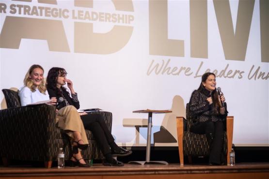 Louisa Vilela speaks while sitting in a chair on the stage at the Lead Live event, while Grace Cantwell and Kasielle Carroll sit in chairs nearby on the stage.